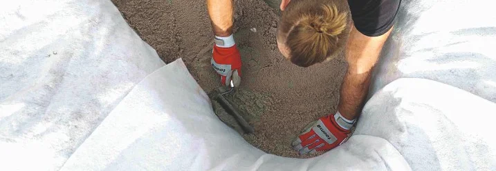 Person verteilt Sand mit Kelle in einem Teich